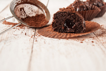 Chocolate chip muffin in brown wax paper. Unwrapped. Cocoa powder in the background