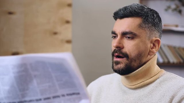 Sleepy bearded man trying to read daily newspaper, boring news, routine life