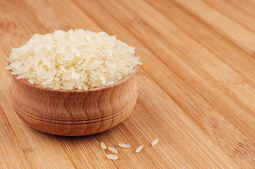 White rice basmati in wooden bowl on brown bamboo board, closeup. Healthy dietary cereals  background.