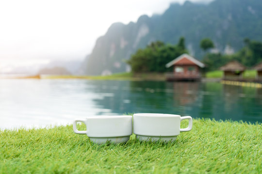 Couple Or Two Coffee Cups On The Grass Over Lake