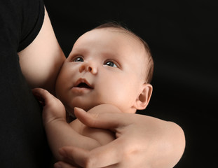 Mother holding newborn on black background, closeup