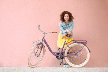 Beautiful young woman with bicycle on color wall background