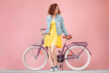 Obraz na płótnie Canvas Beautiful young woman with bicycle on color wall background