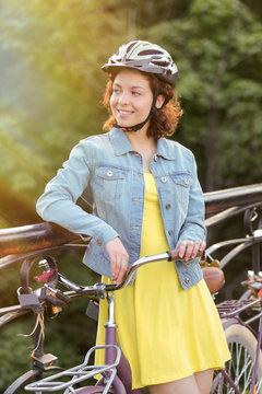 Beautiful young woman with bicycle standing on bridge
