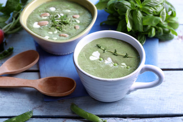 Delicious puree from green peas in cup and bowl on wooden table