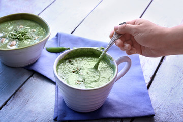 Young woman tasting delicious puree from green peas on table