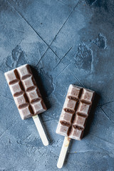 brown chocolate shaped popsicles on wooden stics on gray background, top view, copy space