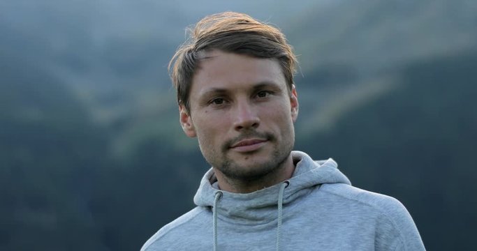 Portrait of man looking at camera from different angles face close up outdoors in mountains 4k. Caucasian confident handsome calm 30s guy sportsman traveler with loving kind brown eyes in grey sweater