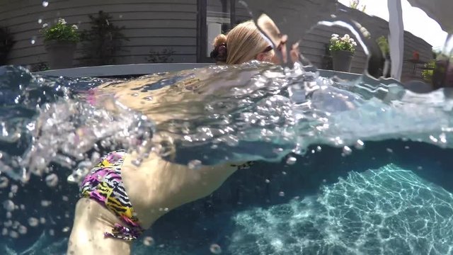 Camera half above and half below water, a beautiful, slim, caucasian woman wearing string bikini swims from left to right. Camera follows her.