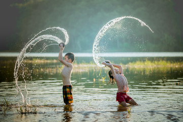 asian children playing splashing water in the river.
