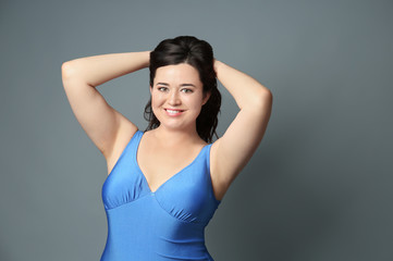 Beautiful overweight woman in blue swimsuit on grey background