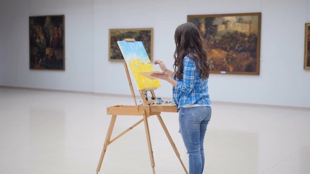 Female fashion painter drawing a picture on easel. 4K.