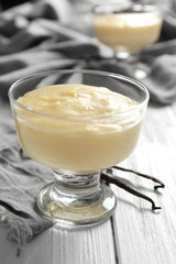 Vanilla pudding in glass dessert bowl on wooden table