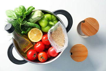 Composition with uncooked quinoa and products in stewpan on white background