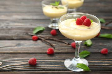 Vanilla pudding served in glass with fresh mint and raspberries on wooden table