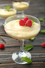 Vanilla pudding served in glass with fresh mint and raspberries on wooden table
