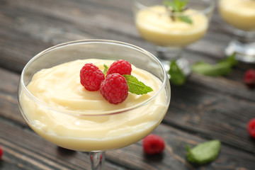 Vanilla pudding served in glass with fresh mint and raspberries on wooden table
