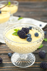 Vanilla pudding served in dessert bowl with blueberries and blackberries on wooden table