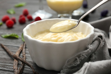 Teaspoon and ceramic bowl with vanilla pudding on wooden table