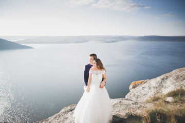 Fototapeta na wymiar Wedding couple kissing and hugging on rocks near blue sea