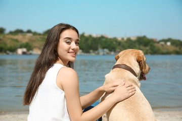 Young woman resting with yellow retriever near river