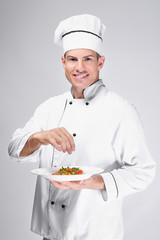 Young male chef holding plate with salad on light background