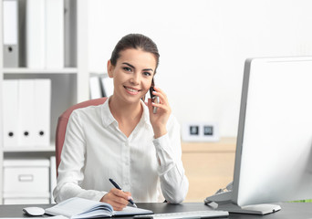 Young female receptionist talking on phone in office - obrazy, fototapety, plakaty