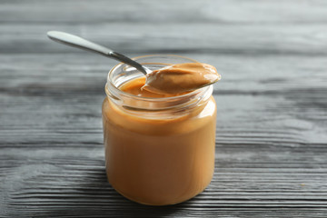 Spoon and glass jar with creamy peanut butter on wooden background