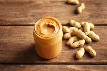 Glass jar with creamy peanut butter on wooden background