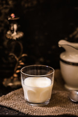 Glass of fresh farm milk with butter cookies stack on sack cloth and spoon by side, rural scene in rustic style and dark background with clay pot, organic breakfast, diary product, copy space for text
