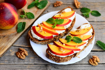 Rye bread sandwiches with soft cream cheese, nectarines, walnuts and mint on a serving plate and on a vintage wooden table. Recipe using rye bread. Closeup