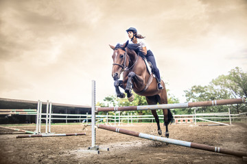 Girl riding a horse, jumping over an obstacle