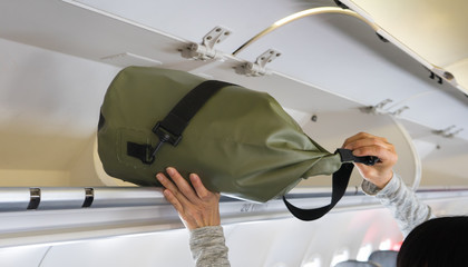 Passenger woman putting luggage into overhead locker on airplane (Selective focus)