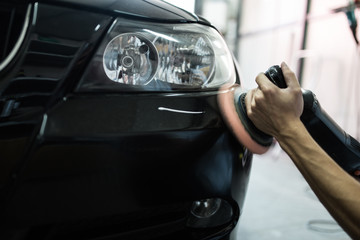 Car detailing - Hands with orbital polisher in auto repair shop. Selective focus.