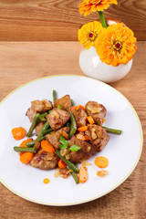 Beef liver with vegetables: carrot, onion and green beans on white plate, vertical