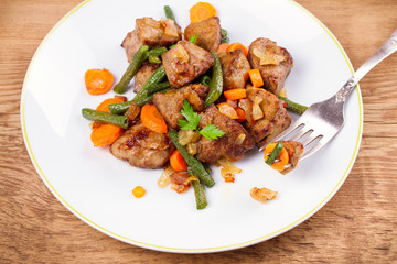 Beef liver with vegetables: carrot, onion and green beans on white plate, horizontal