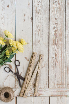 Flores amarillas con tijeras y ovillo de cuerda y metro de carpintero sobre fondo de tablones de madera envejecida