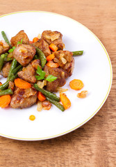 Beef liver with vegetables: carrot, onion and green beans on white plate, vertical