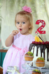 Girl birthday. A little white-haired girl of two years is trying a birthday cake. Little girl celebrating second birthday.