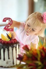 Girl birthday. A little white-haired girl of two years is trying a birthday cake. Little girl celebrating second birthday.