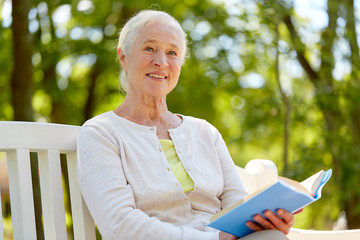happy senior woman reading book at summer park