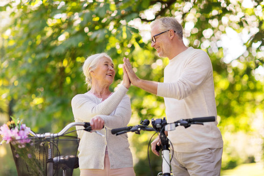 senior couple with bikes making high five at park
