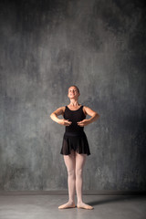 Fototapeta na wymiar Young beautiful ballerina in a black dress, pointe shoes standing in a dance position in front of a ballet in a dark dance studio