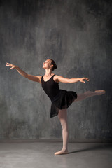 Young beautiful ballerina in a black dress, pointe shoes standing in a dance position in front of a ballet in a dark dance studio