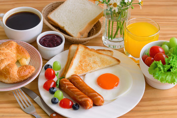 Homemade breakfast with sunny side up fried egg toast sausage fruits vegetable strawberry jam and orange juice in top view. Delicious homemade american breakfast concept for background or wallpaper.