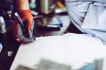 Senior man in workshop. Man writing obligations in his notes. Close up.