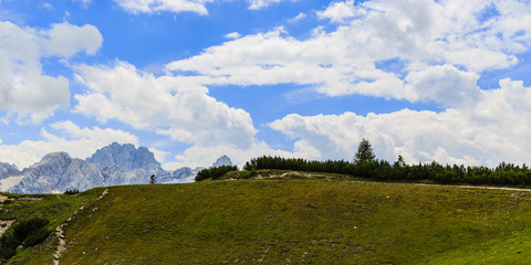 Tourist cycling in Cortina d'Ampezzo, stunning rocky mountains on the background. Woman riding MTB...