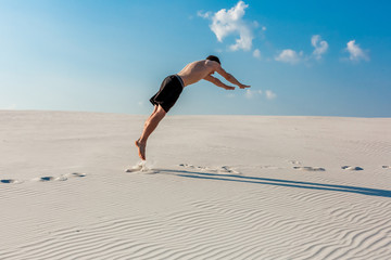 Young man jumping on the beach with white sand and bright blue sky