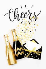 Card with word Cheers with black and gold champagne bottles. Flat lay, top view.