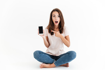 Shocked brunette woman showing blank smartphone screen